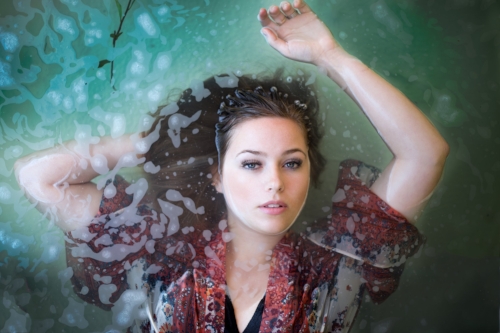 A woman is standing in the water with her arms up.