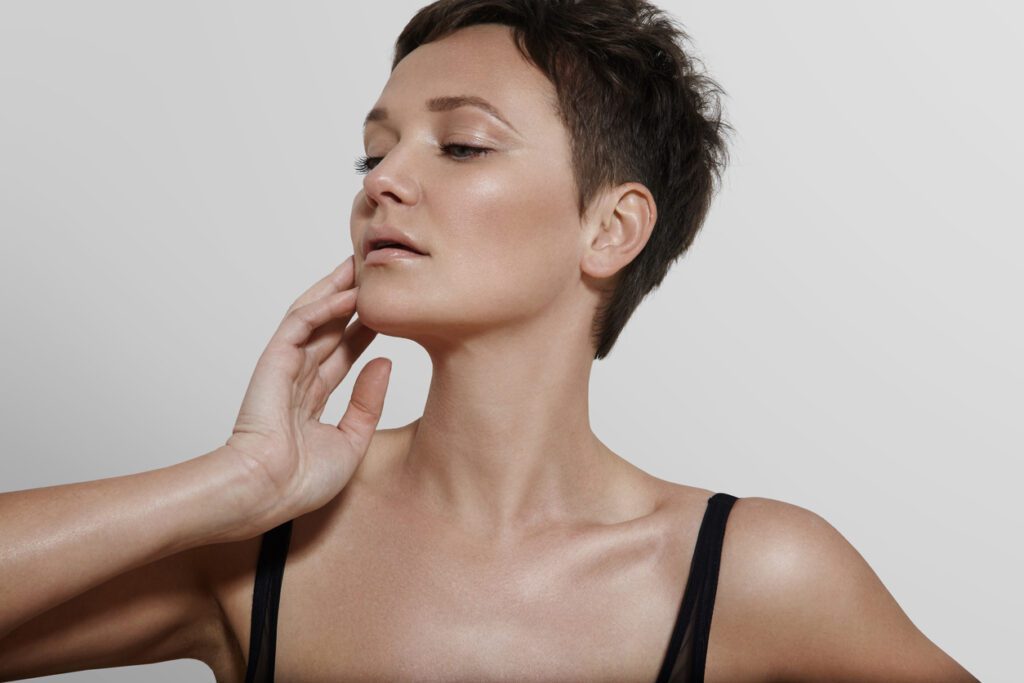 A woman with short hair is touching her face.