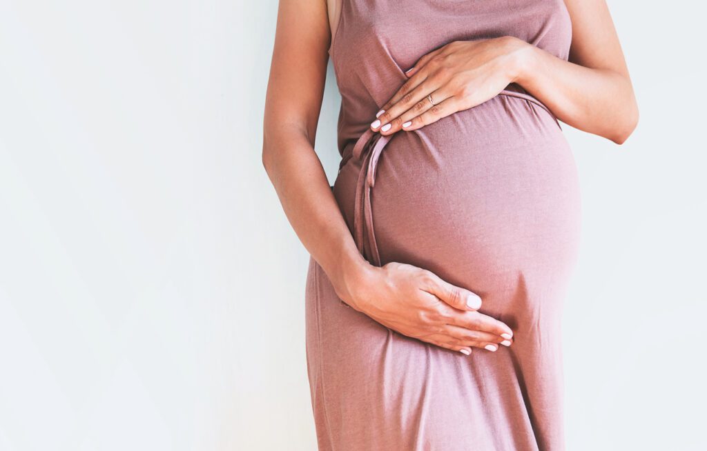 A pregnant woman in a pink dress holding her belly.